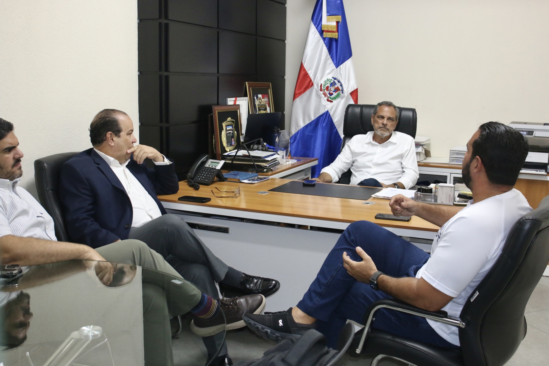 Jepssy Beltré (Fanático de la Patria) conversa con Junior Noboa, director de la Oficina del Comisionado Nacional de Béisbol, y Franklin de la Mota, viceministro de deportes. Aparece también Eduardo Melo.